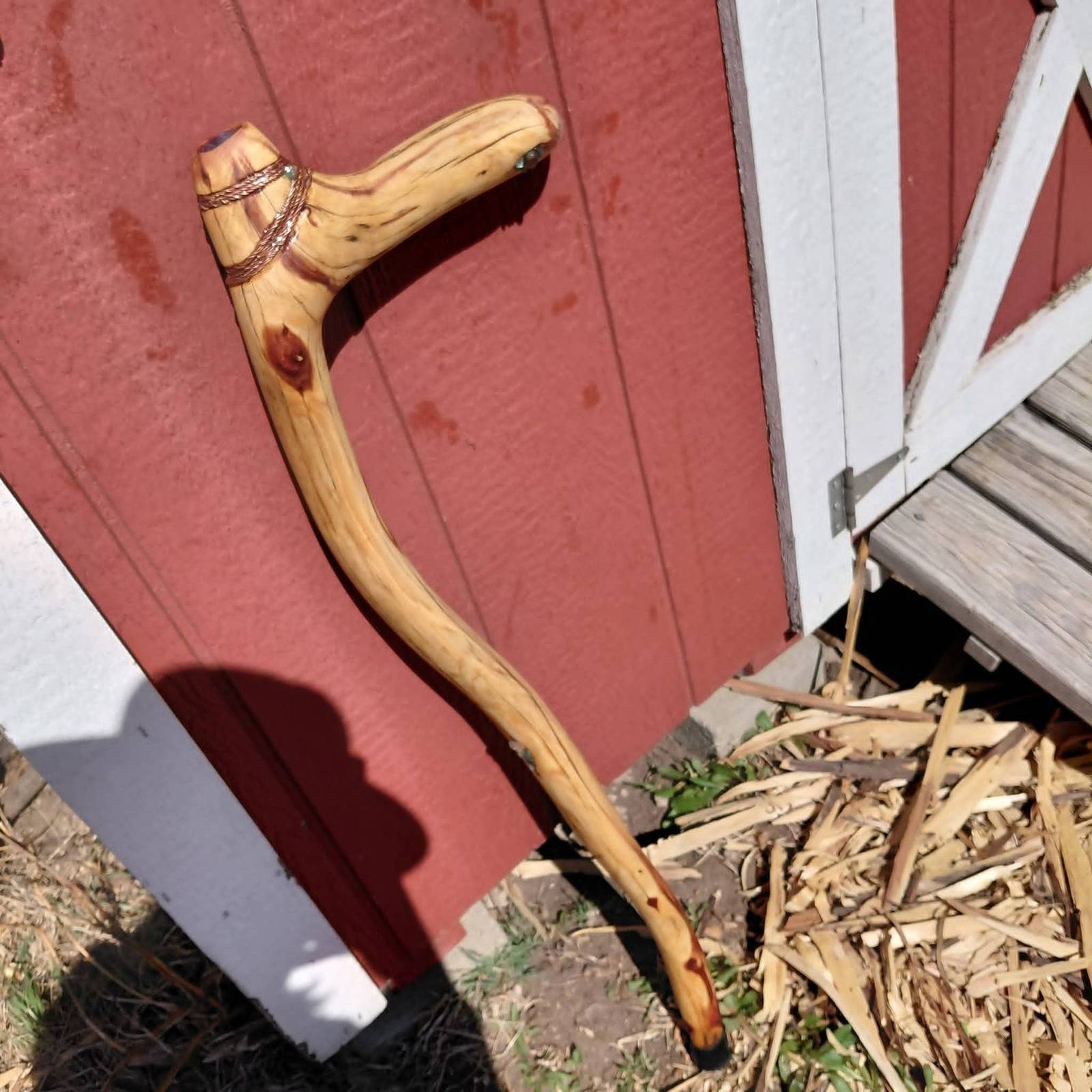 An eastern red cedar cane with a twisted copper wire wrap at the handle, against a red barn wall
