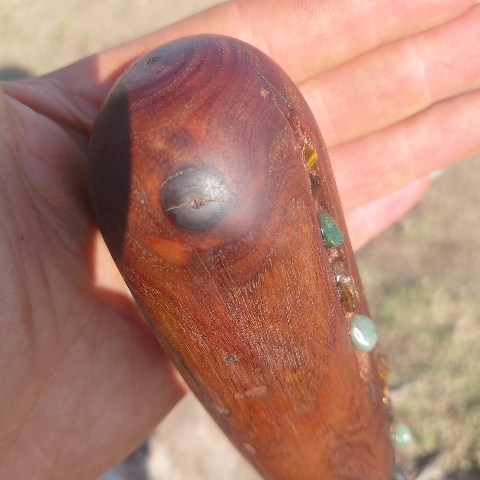 A dark wood handle with green aventurine and tiger eye set along its length, held in the palm