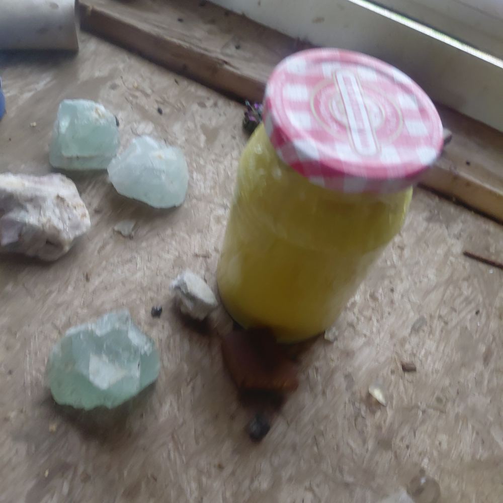 A jelly jar of pale yellow homemade wood finish on a chipboard bench beside pieces of pale green rough stone.