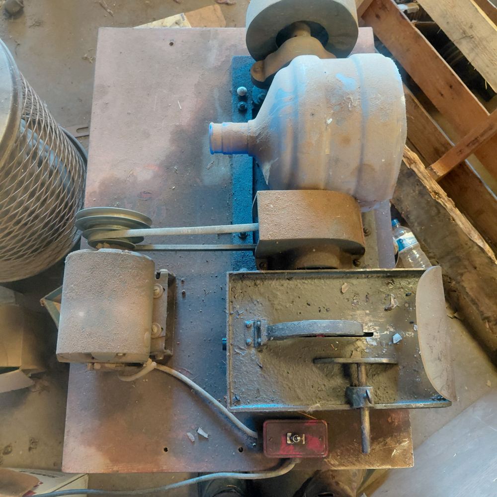 An old lapidary unit seen from above: a belt-driven arbor with a grinding wheel, a cast trim-saw table with a toggle switch, a small motor and pulley, all on a plywood base.