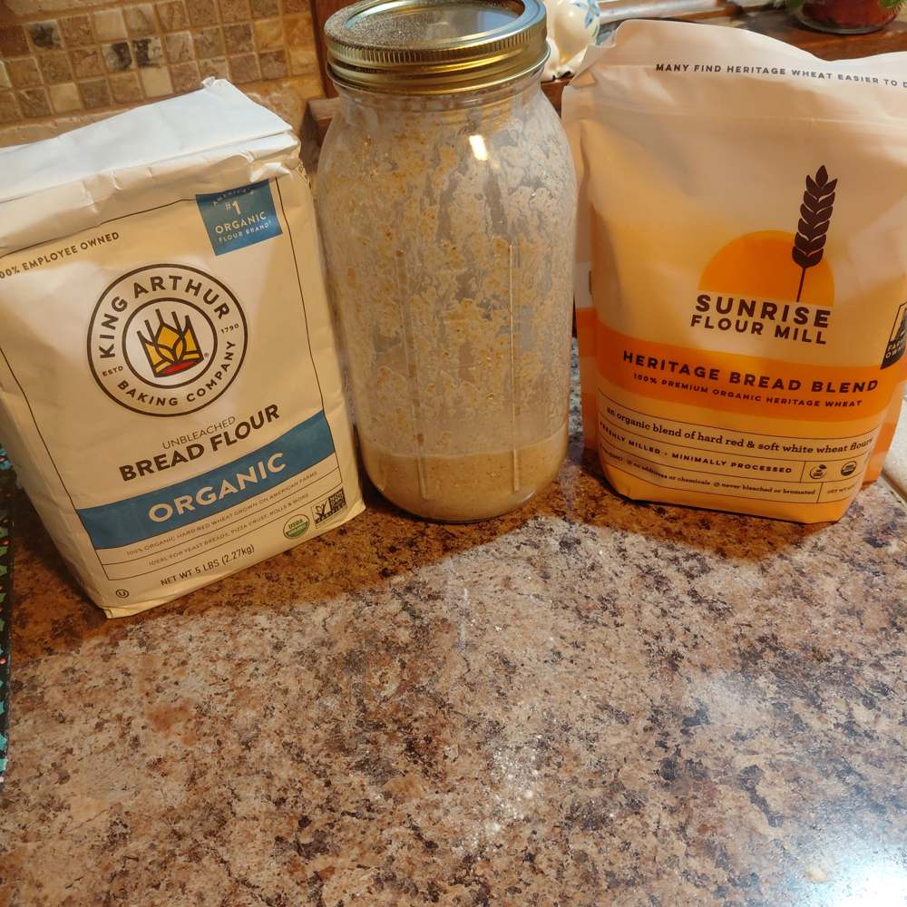 A quart jar of active sourdough starter on a kitchen counter between two bags of bread flour.